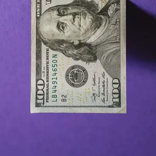 Billede af en 100 dollars sedel med portræt af Benjamin Franklin, placeret på en lilla baggrund.
