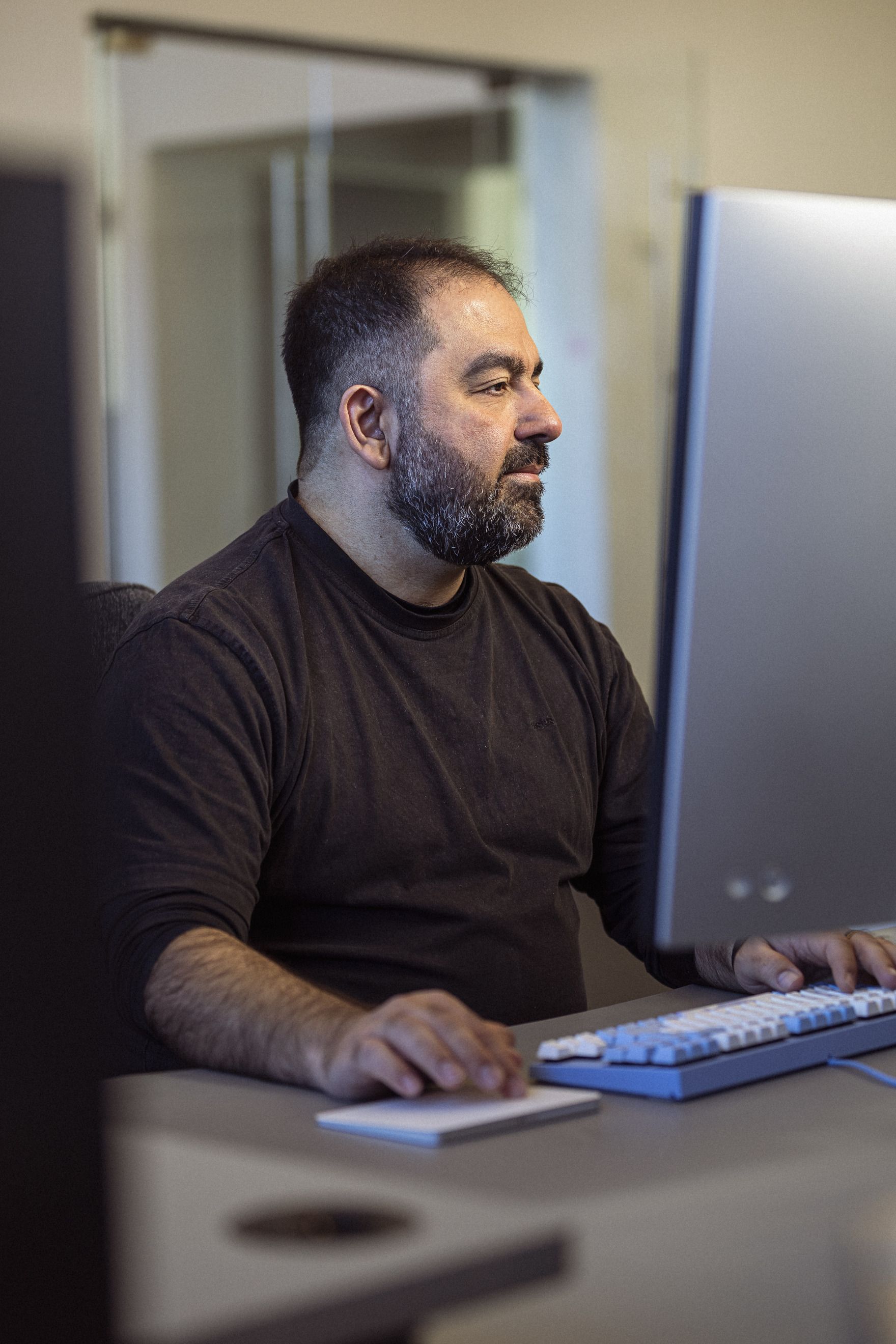 Mand med skæg arbejder koncentreret ved en computer i et moderne kontormiljø.