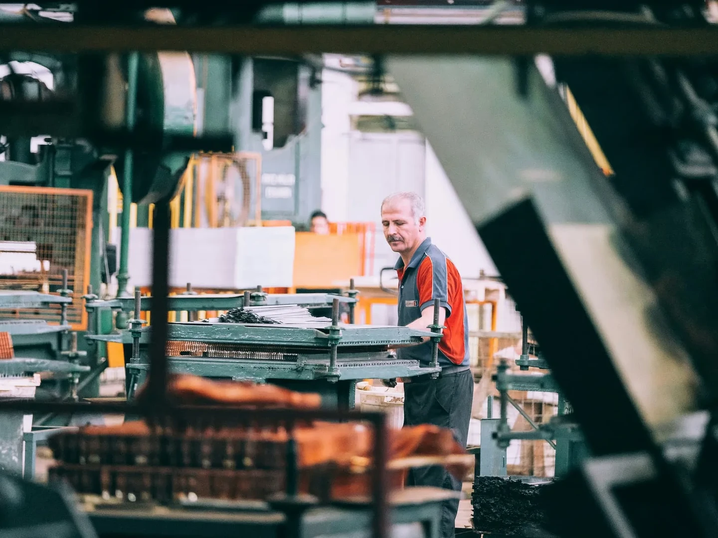 En medarbejder i en fabrik arbejder ved maskinerne, omgivet af industrielle værktøjer og udstyr i en travl produktionshal.