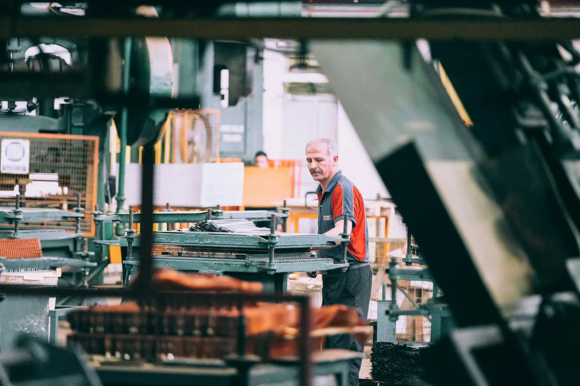 En medarbejder i en fabrik arbejder ved maskinerne, omgivet af industrielle værktøjer og udstyr i en travl produktionshal.