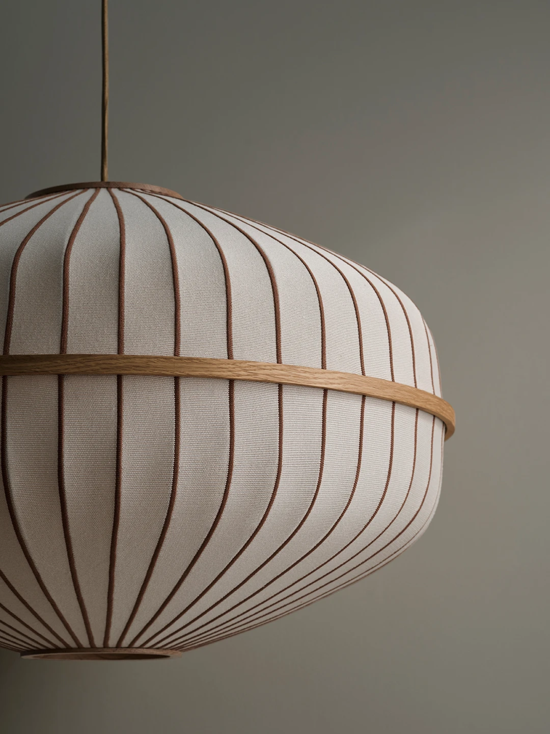 Lysende lampe med tekstiloverflade i hvidt og beige striber, hængende fra loftet mod en neutral baggrund.