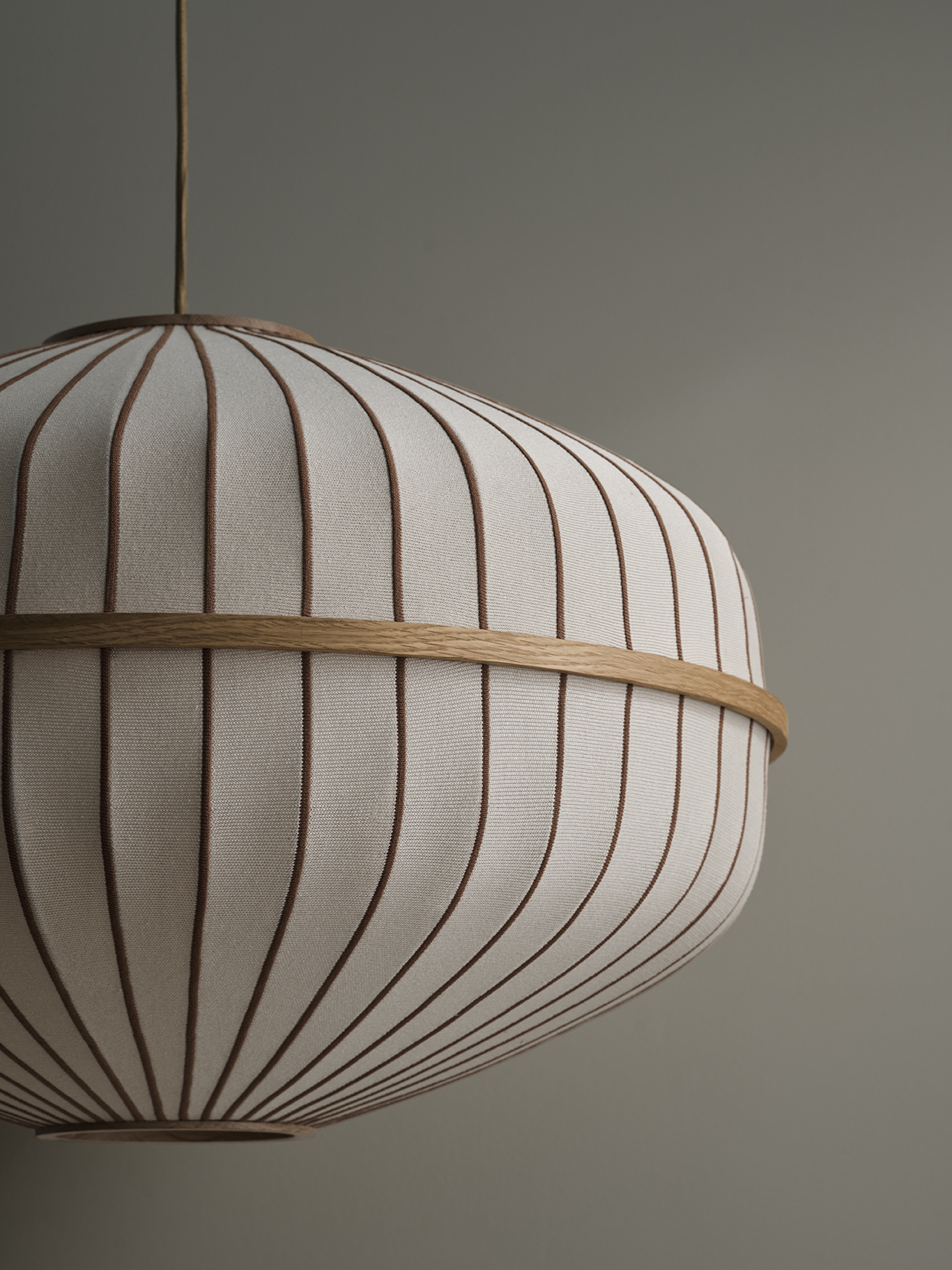 Lysende lampe med tekstiloverflade i hvidt og beige striber, hængende fra loftet mod en neutral baggrund.
