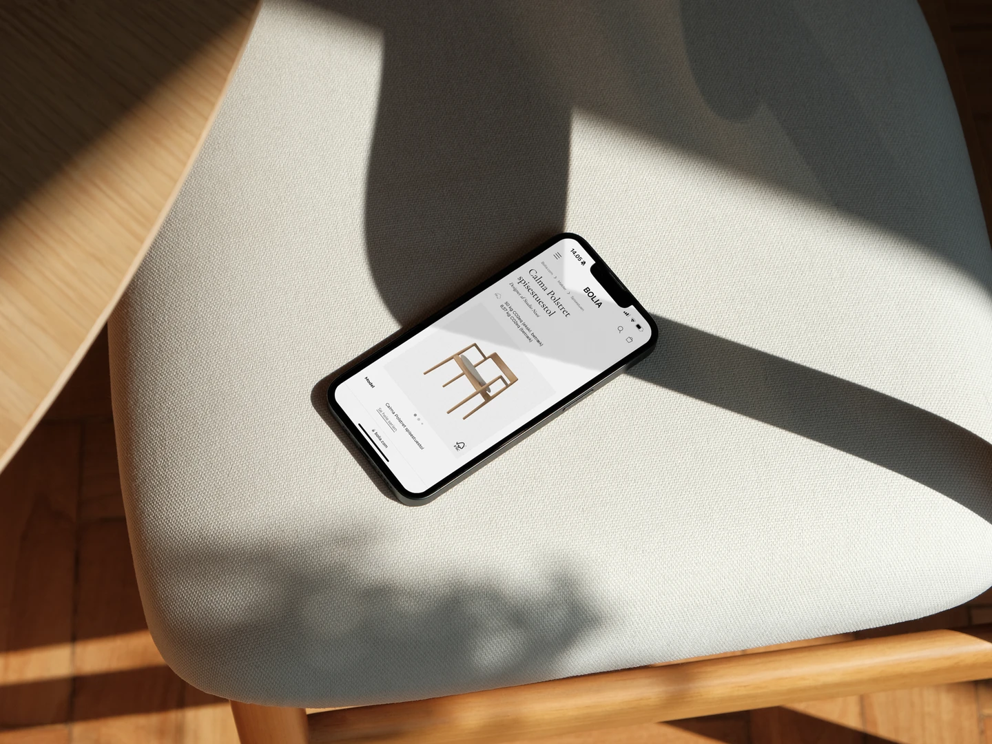En smartphone ligger på en beige stol med skygger, viser en hjemmeside med en stol og indkøbsmuligheder.