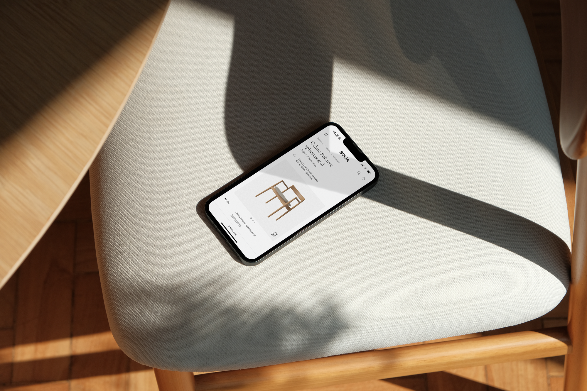 En smartphone ligger på en beige stol med skygger, viser en hjemmeside med en stol og indkøbsmuligheder.