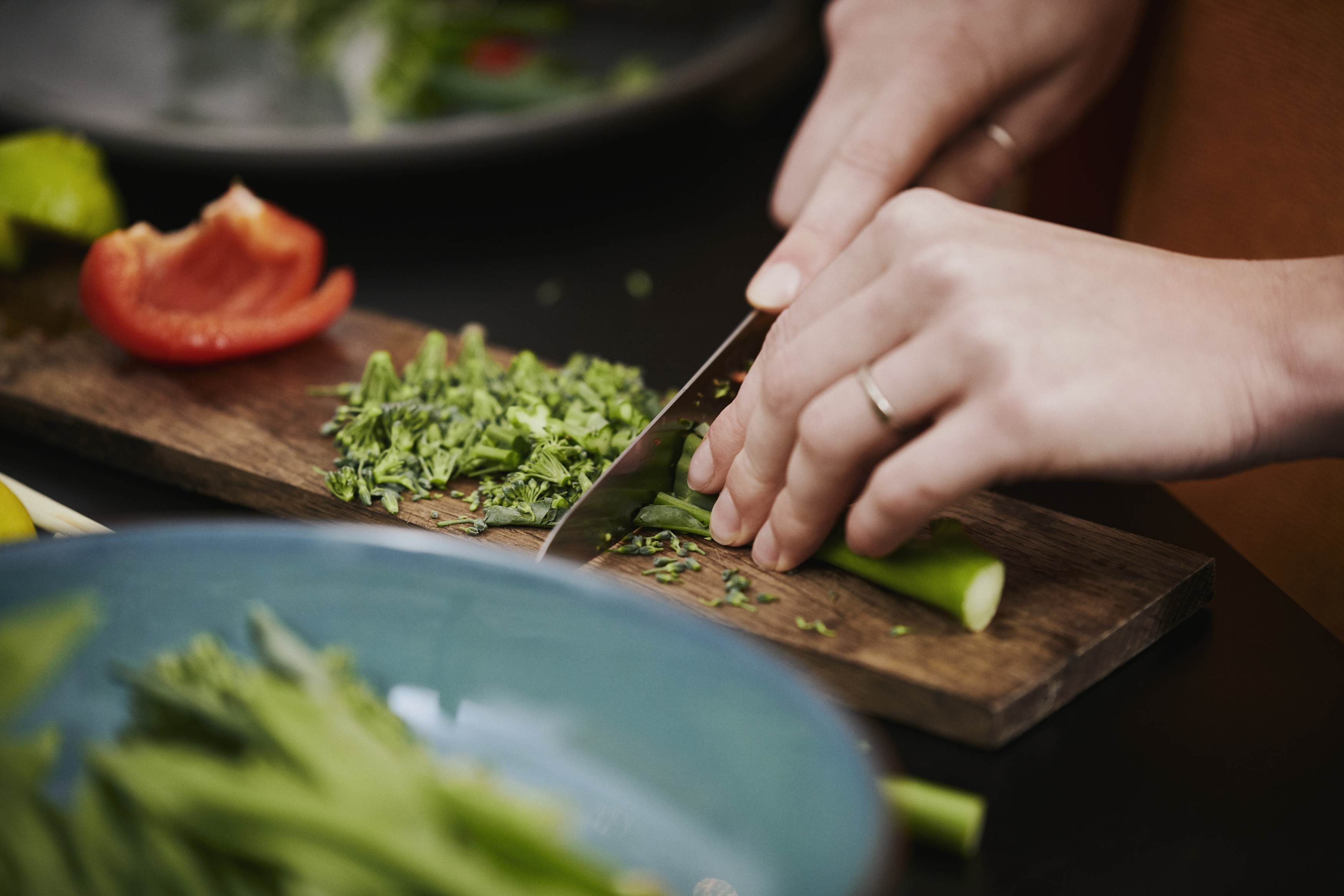 På billedet ses en masse forskellige friske grøntsager, og en formodet kvinde er i gang med at skærer asparges broccoli med en størrer kniv.