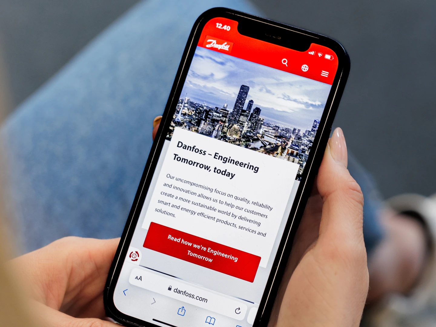 A person holding a smartphone displaying the Danfoss website, featuring a city skyline and text about engineering solutions for a sustainable future.