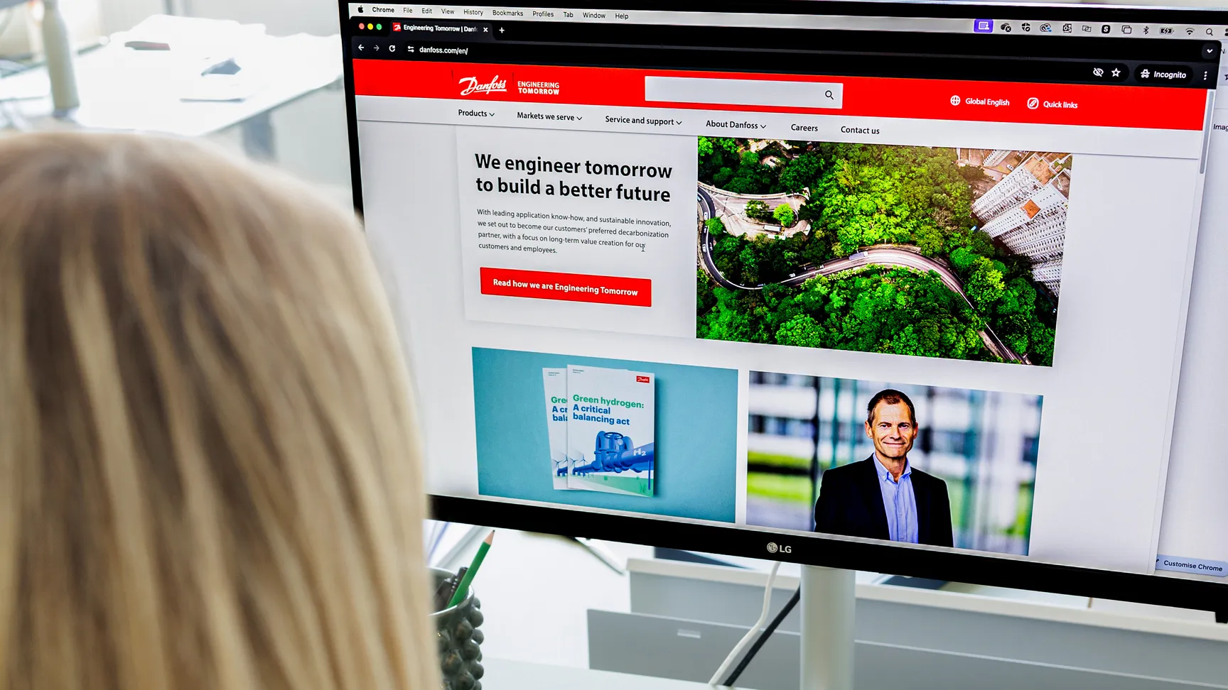 A person sitting at a desk, focusing on a computer screen displaying the Danfoss website, showcasing a message about engineering for a sustainable future, with images of greenery and a professional figure highlighted below.