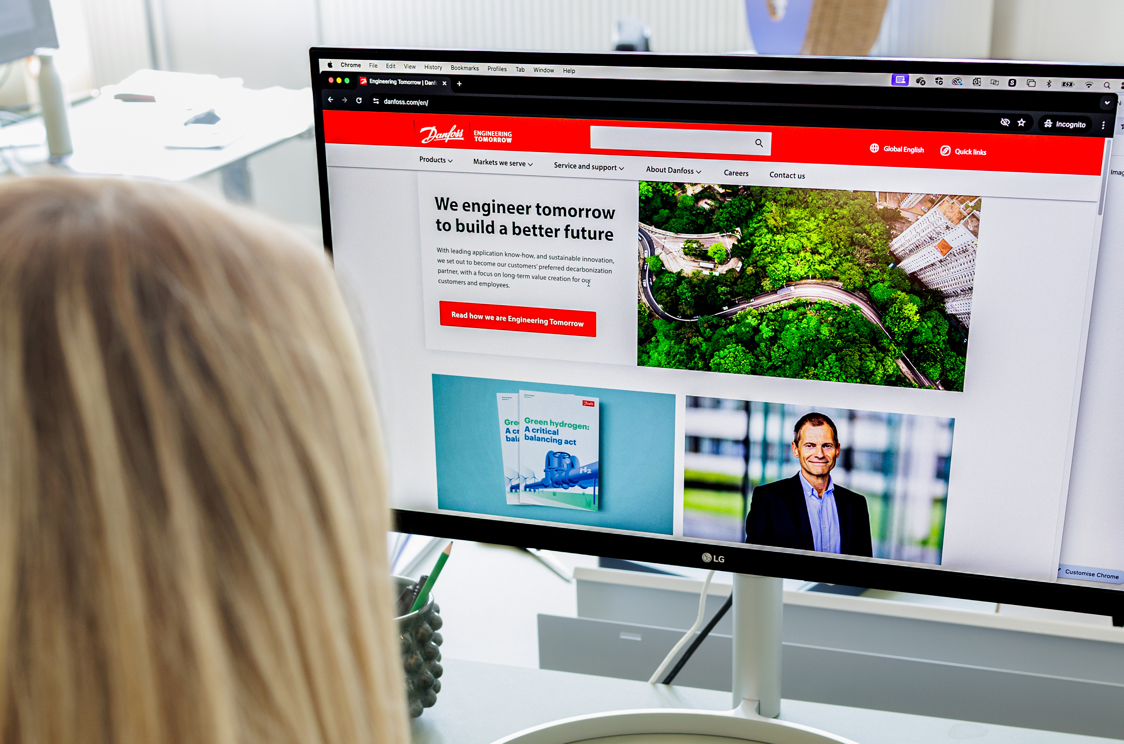 En person ser på Danfoss hjemmeside på en computer, der viser oplysninger om bæredygtig innovation og fremtidige løsninger med billeder af grønne områder og produkter.