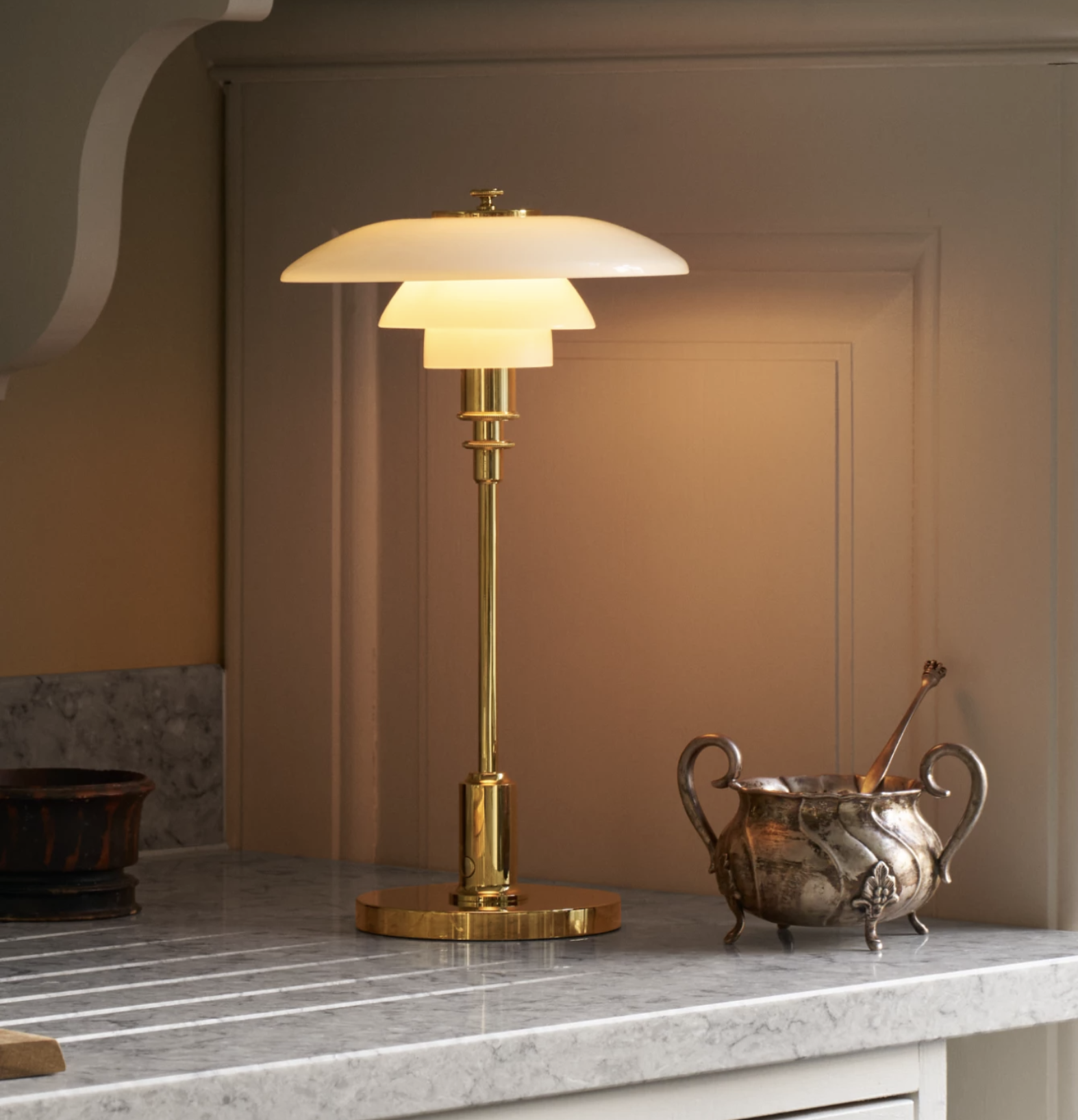 Elegante bordlampe med en kombination af guld og opalglas, placeret på en marmoroverflade ved siden af en antik sølvskål.