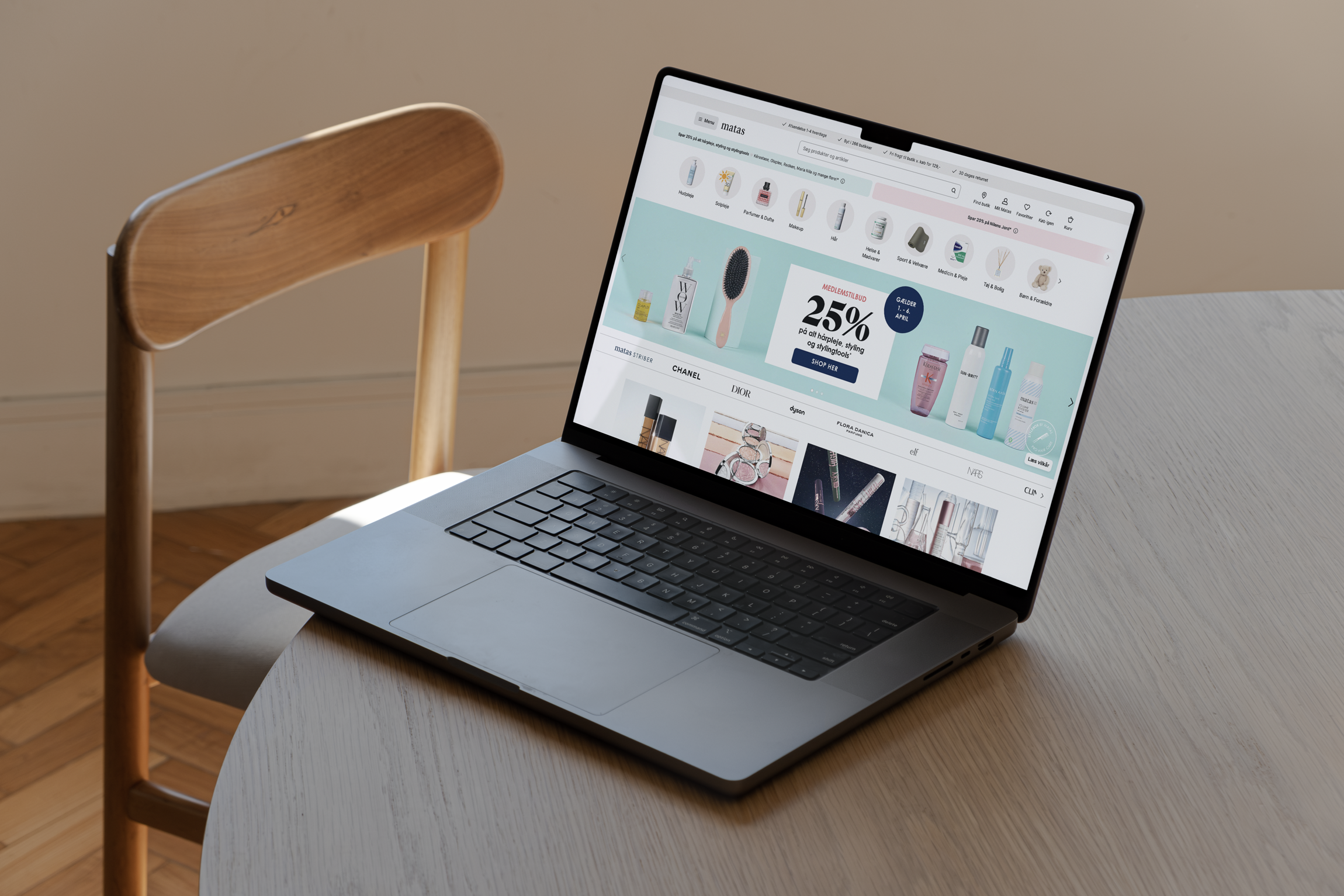 En bærbar computer står på et rundt bord med en træstol i baggrunden, viser en kosmetik-webshop med en kampagne på 25% rabat.