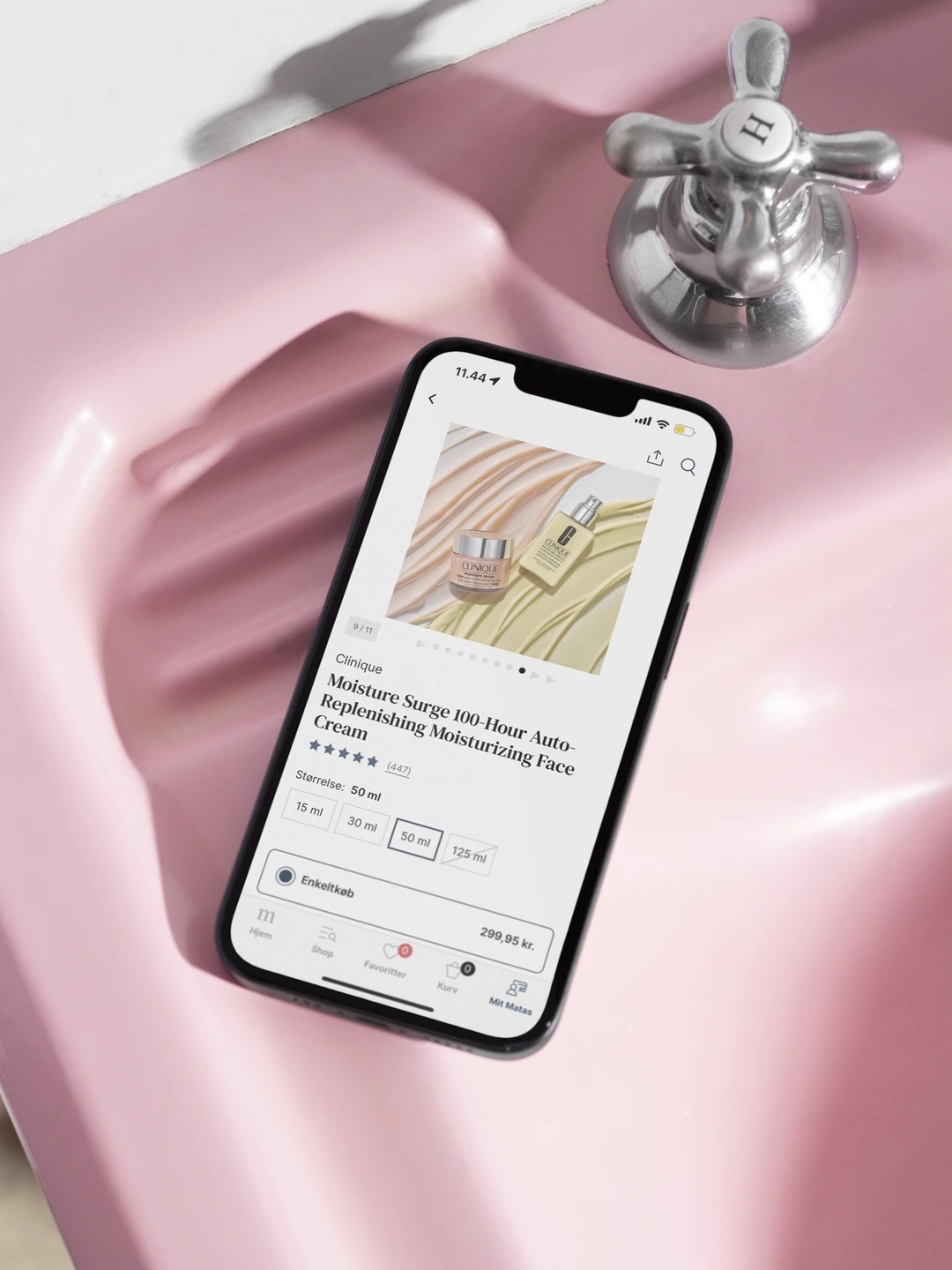 A smartphone displaying a product page for Clinique's Moisture Surge 100-Hour Auto-Replenishing Moisturizing Face Cream, placed on a pink sink with a silver faucet in the background.