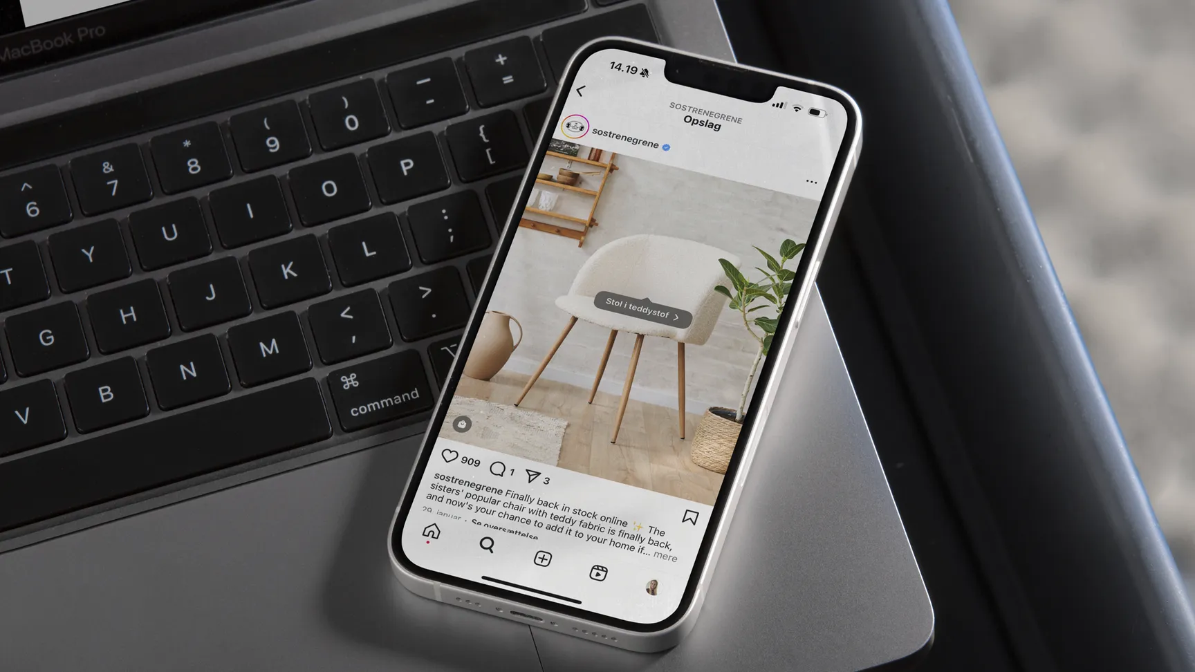 Smartphone på et bord, der viser et Instagram-opslag fra Søstrene Grene med en stol i teddy-stof og en plante i baggrunden.