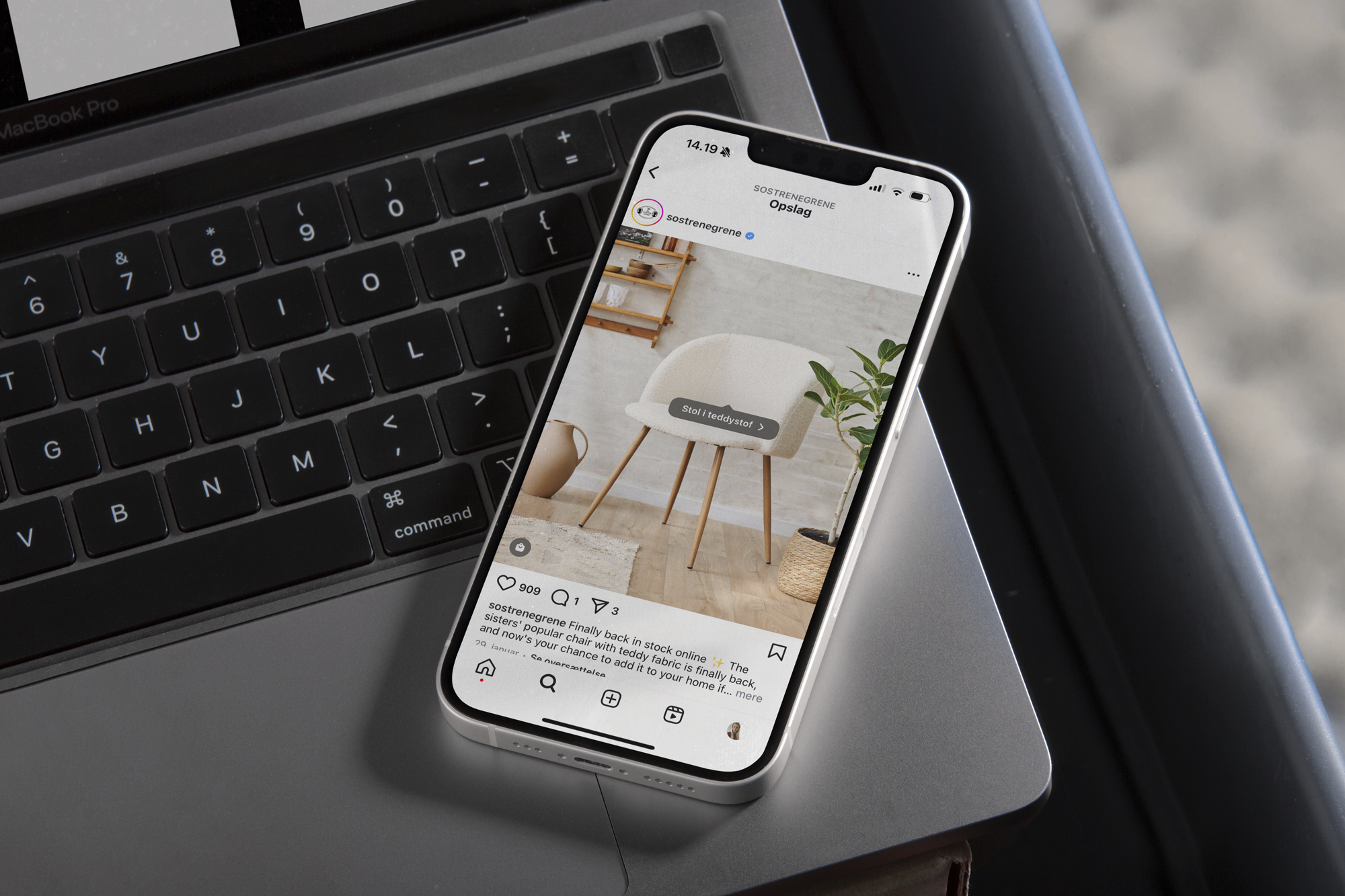 Smartphone på et bord, der viser et Instagram-opslag fra Søstrene Grene med en stol i teddy-stof og en plante i baggrunden.