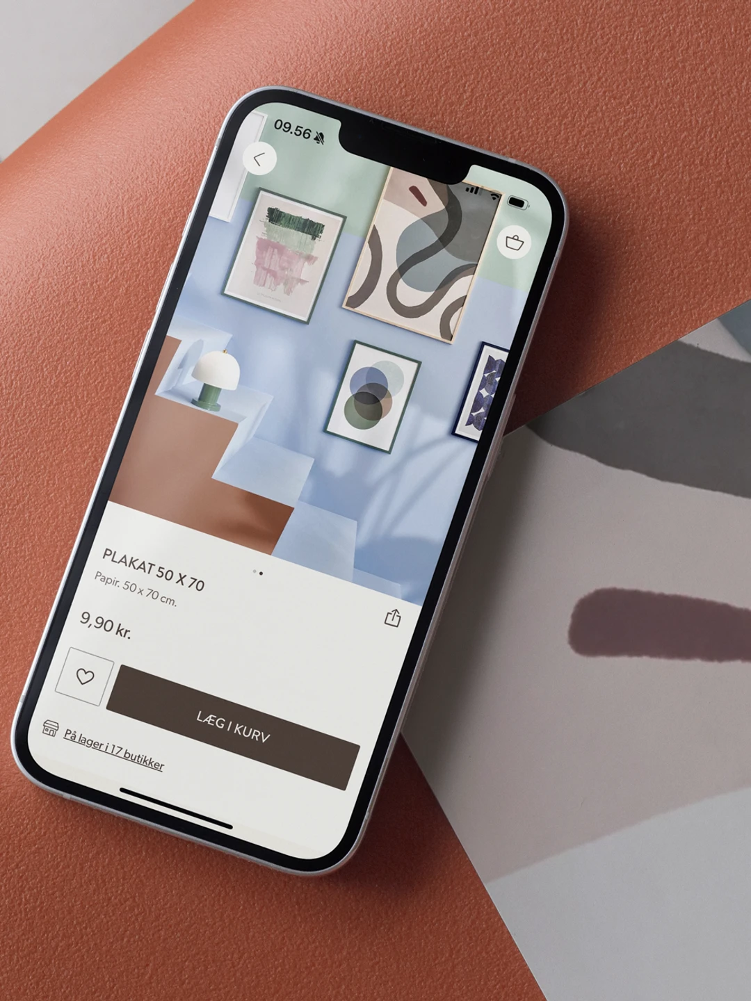 A smartphone displaying artwork and a product listing for a poster titled "PLAKAT 50 X 70" on a textured orange surface, with an abstract background design.