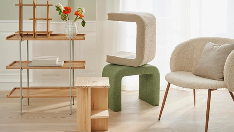 En moderne stue med en træhylde, en blød, geometrisk stol i beige og grøn farve, en lille træbord med to rum og en vase med farverige blomster.