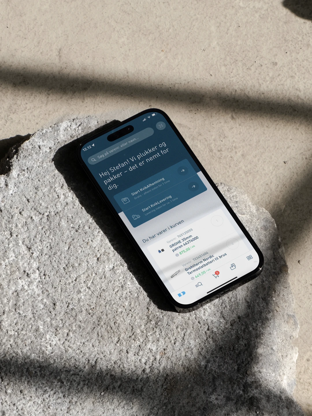 Et smartphone-display viser en velkomstbesked og muligheder for at starte kursusmoduler, placeret på en ru, grå overflade med dybe skygger.