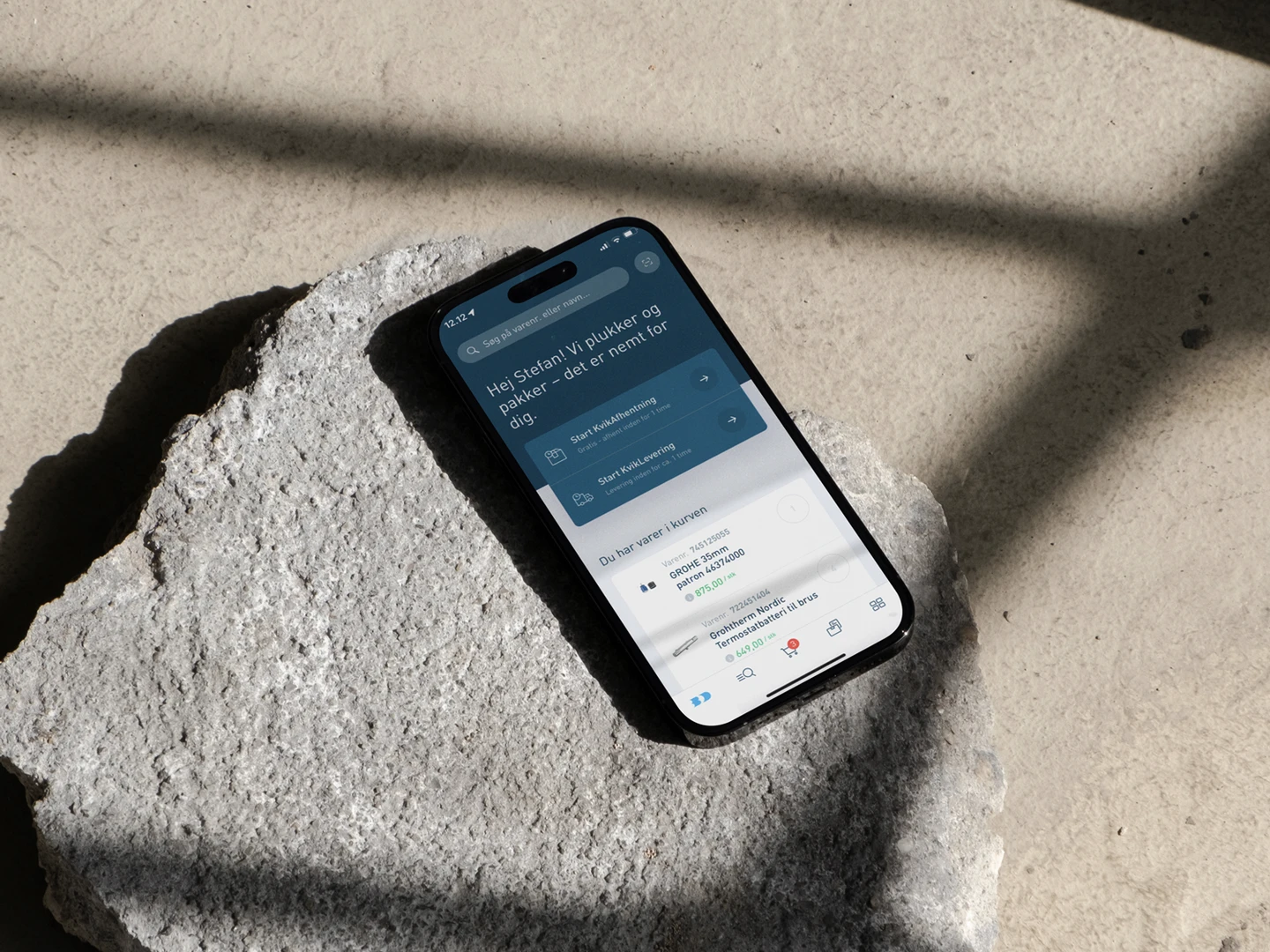 A smartphone displaying a mobile application interface resting on a textured stone surface, with soft shadows and natural light highlighting the device.