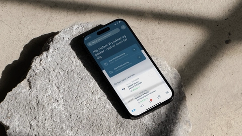 Et smartphone-display viser en velkomstbesked og muligheder for at starte kursusmoduler, placeret på en ru, grå overflade med dybe skygger.
