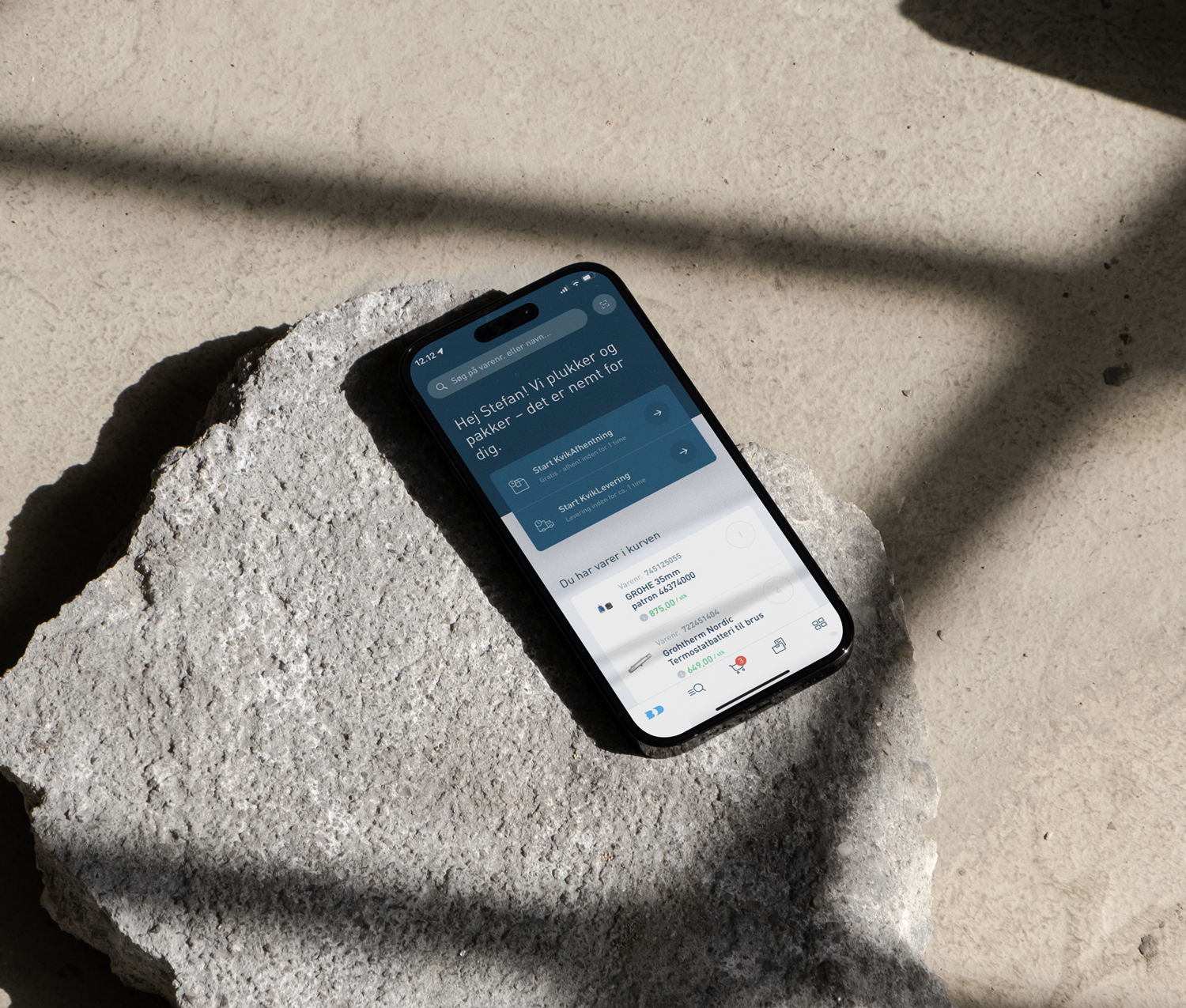 Et smartphone-display viser en velkomstbesked og muligheder for at starte kursusmoduler, placeret på en ru, grå overflade med dybe skygger.