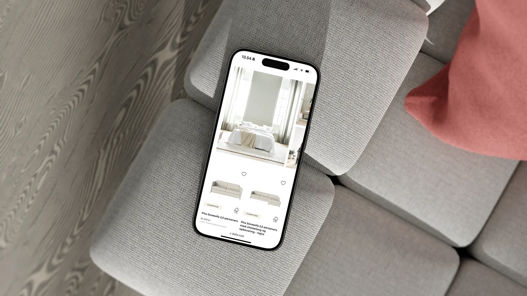Mobiltelefon, der viser en møbelshop-side med billeder af sofaer, ligger på en grå sofadag.