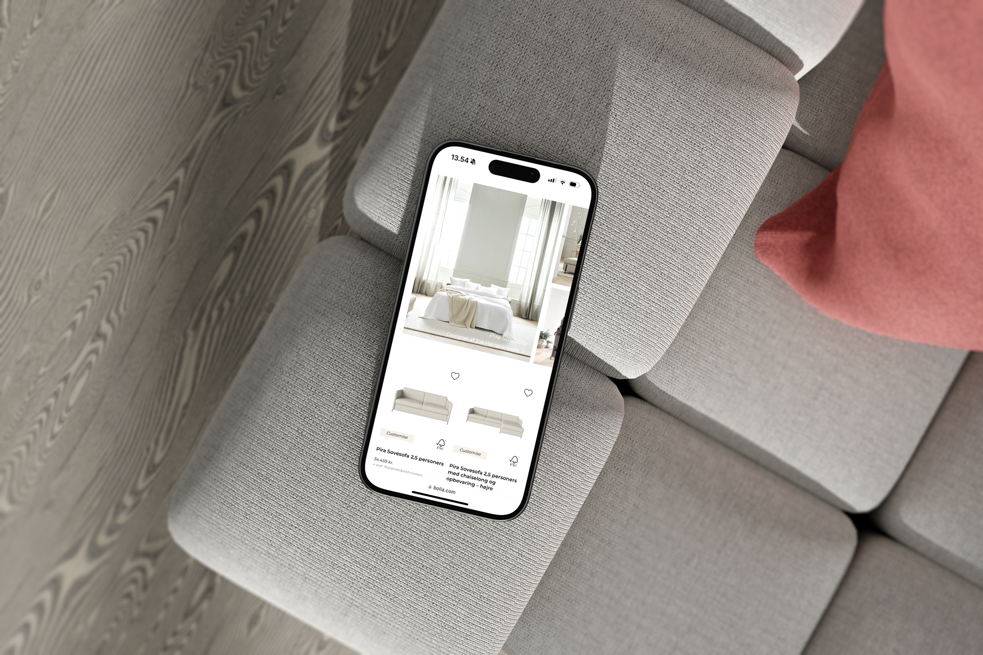 Mobiltelefon, der viser en møbelshop-side med billeder af sofaer, ligger på en grå sofadag.