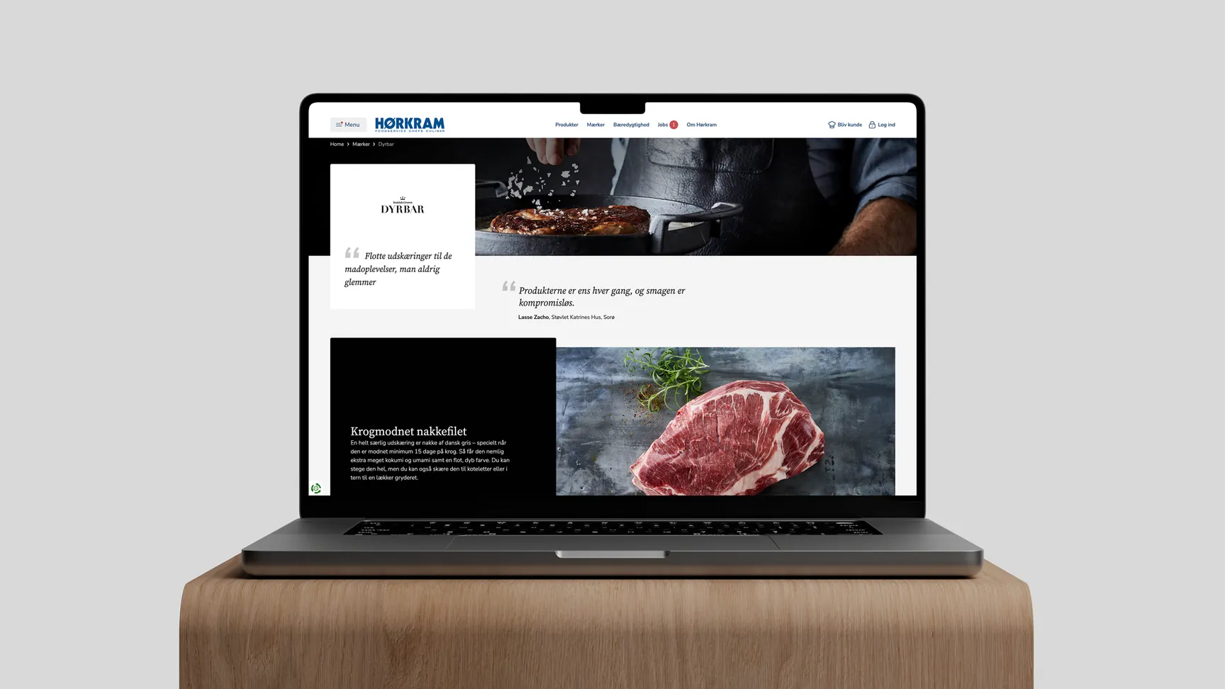 A laptop displaying a webpage with quotes about meat products, accompanied by an image of a raw steak and herbs, set on a wooden surface.