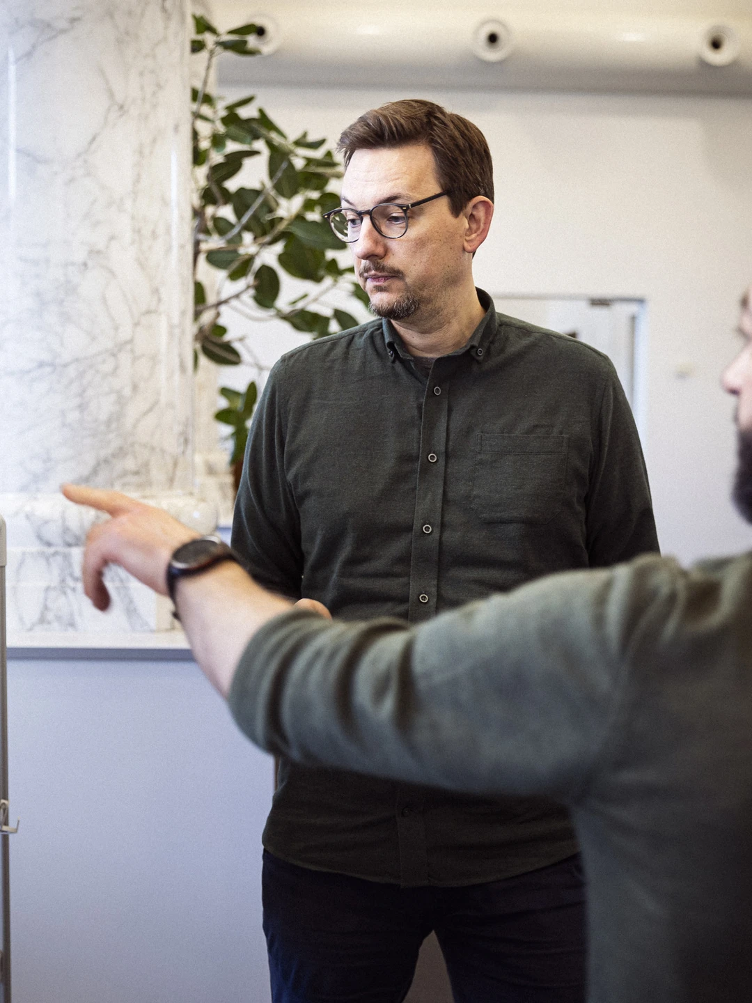 To mænd i en kontormiljø diskuterer over en whiteboard, hvor den ene mand peger og den anden ser opmærksomt på tavlen.
