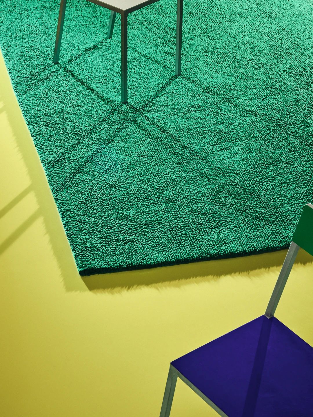 large green carpet on a yellow lacquered floor, with a blue chair placed slightly off-center in the picture