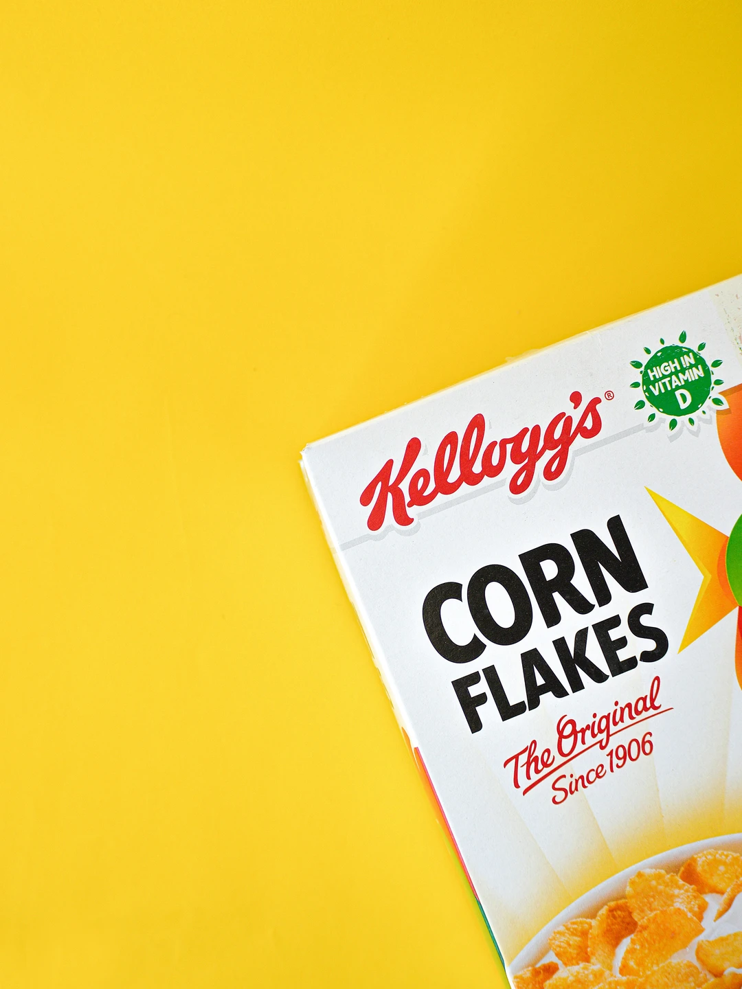 Kellogg's Corn Flakes emballage på en gul baggrund, med teksten "The Original Since 1906" og iconet "High in Vitamin D".