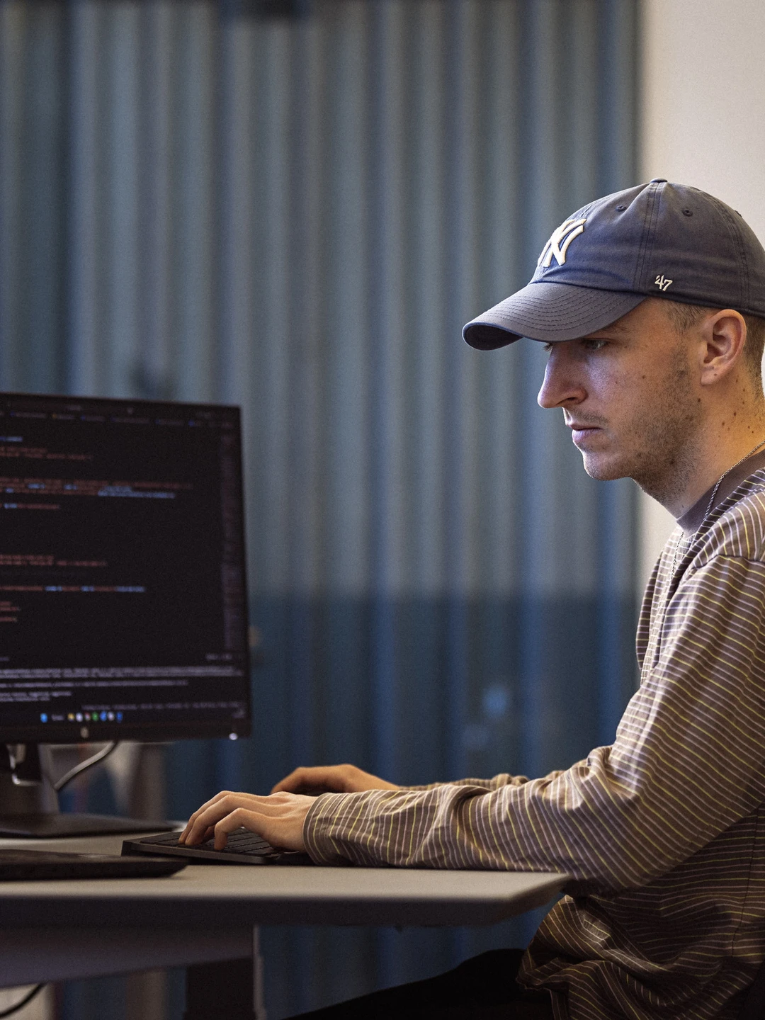 En mand i kasket arbejder koncentreret ved en computer med flere skærme, der viser programmeringskode.