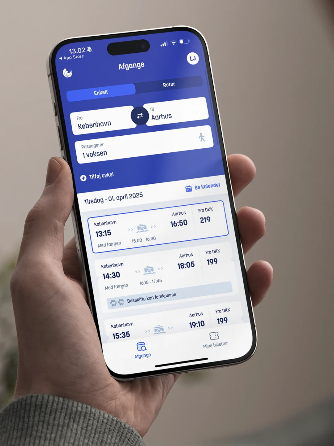 En person holder en smartphone med en rejseapp, der viser afgange fra København til Aarhus, herunder dato, tidspunkt og billetpris.
