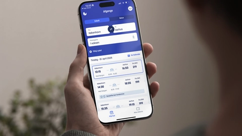 En person holder en smartphone med en rejseapp, der viser afgange fra København til Aarhus, herunder dato, tidspunkt og billetpris.