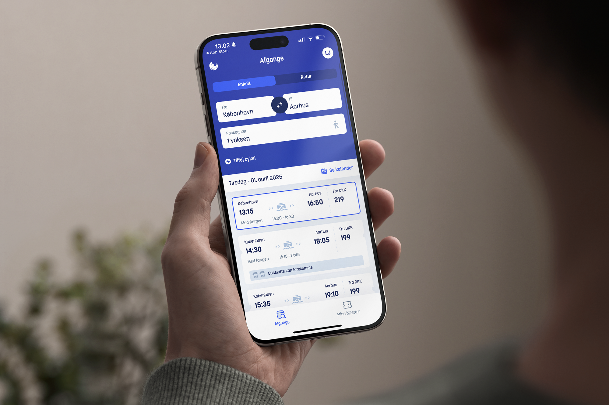 En person holder en smartphone med en rejseapp, der viser afgange fra København til Aarhus, herunder dato, tidspunkt og billetpris.