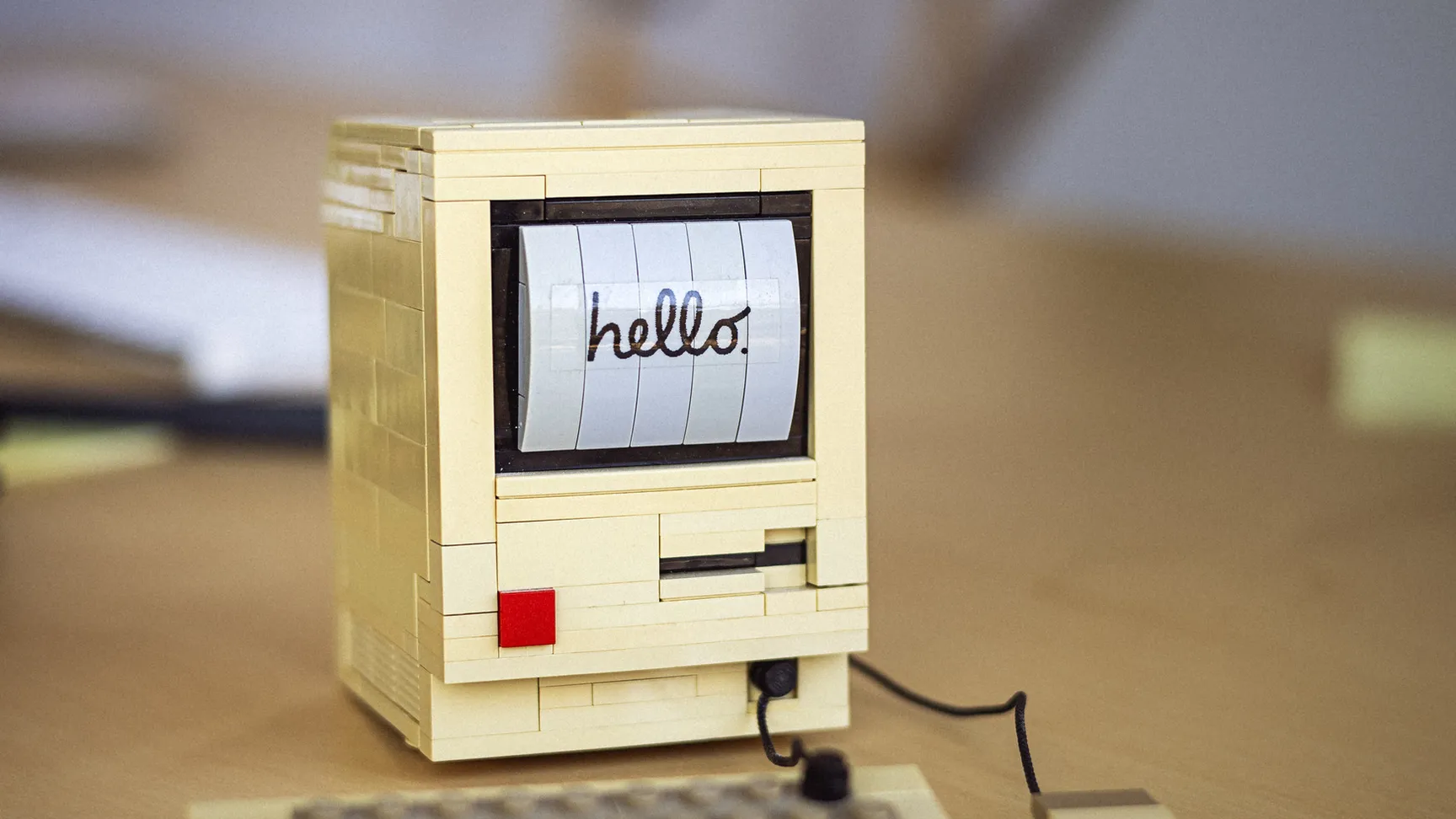 LEGO-inspireret computer med teksten "hello" på skærmen, placeret på et skrivebord med en mus og tastatur ved siden af.
