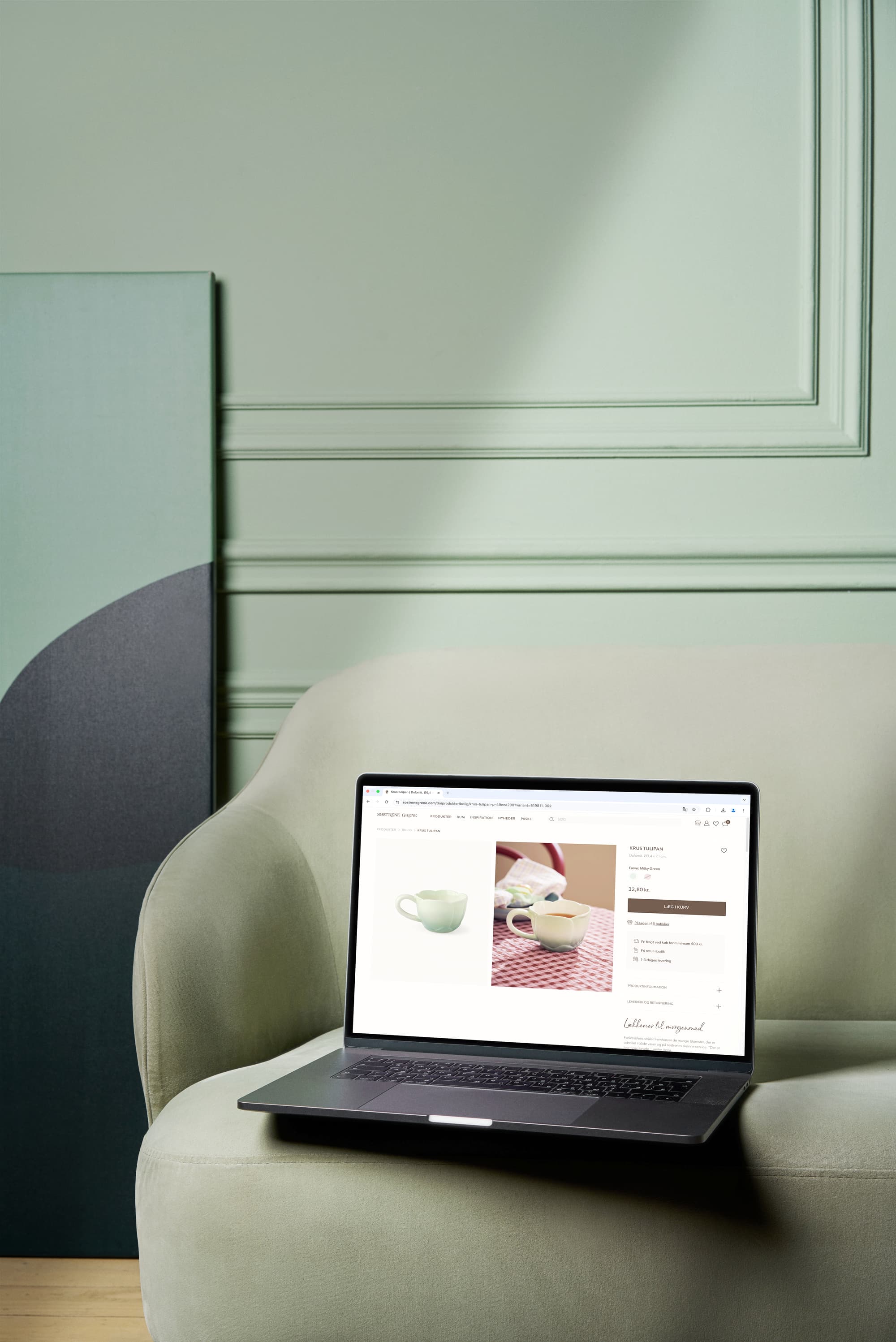 Billede af en bærbar computer, der viser et produktbillede af en keramisk kande på en rødternet dug, placeret på en grøn sofa med en dekorativ vægplade i baggrunden.