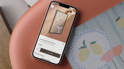 Smartphone der viser en A3 plakat med blomsterdesign i en træramme, placeret på en rødbrun overflade.