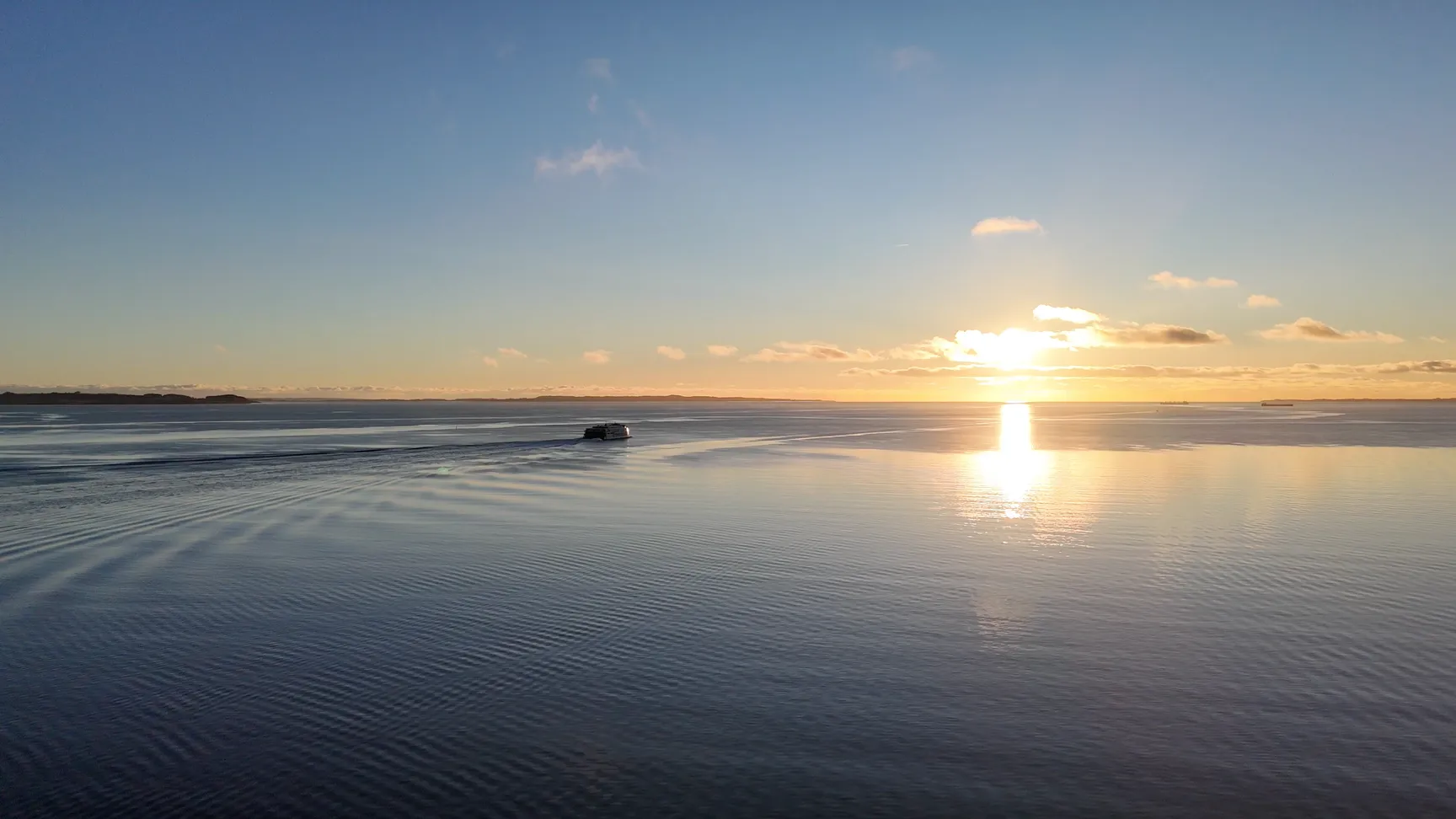 A serene ocean view at sunset with gentle waves reflecting the warm colors of the sky, and a small boat navigating through the calm water.