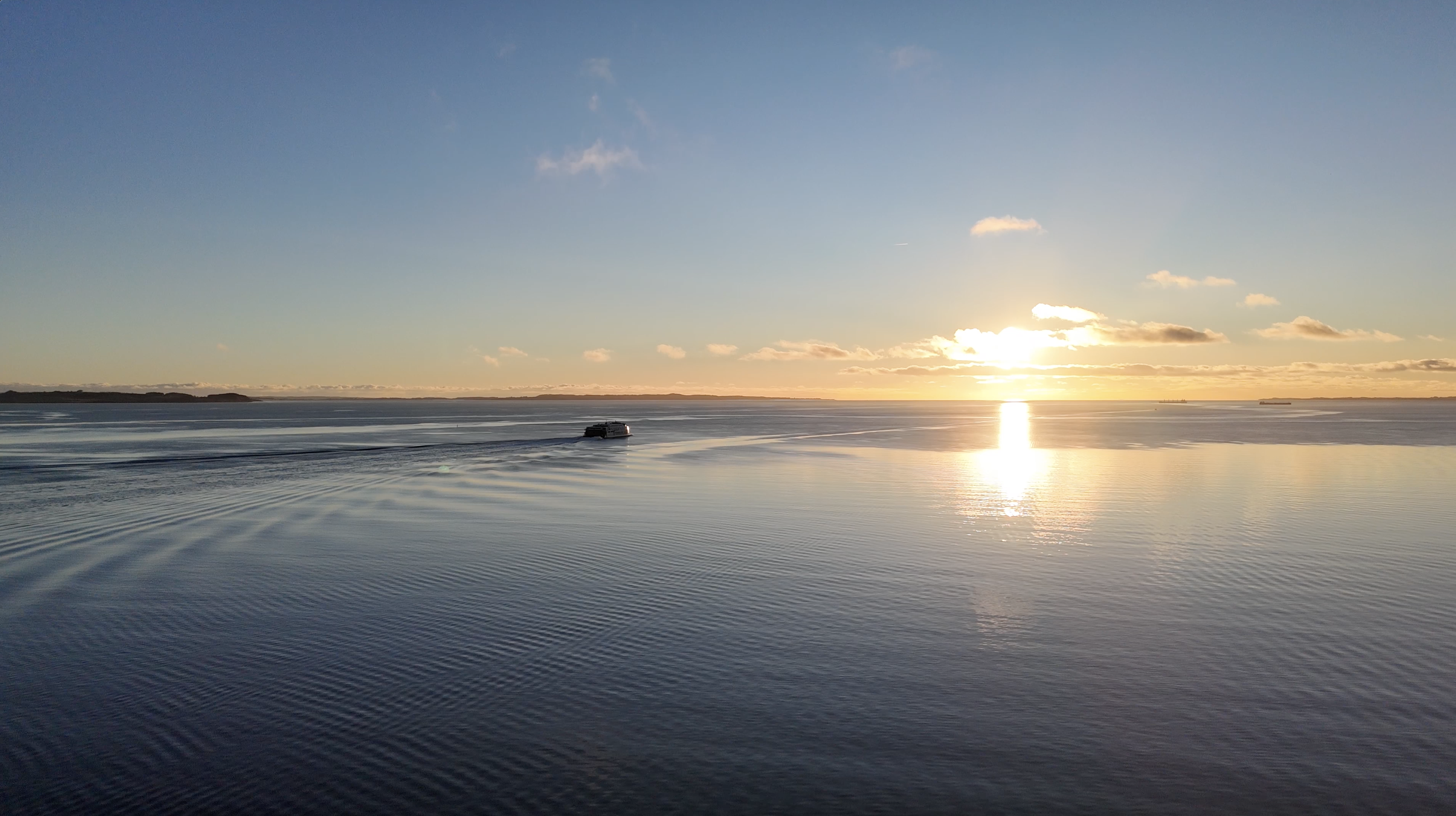 en solnedgang ud over vandet mens man på vandet ser ern færge sejle forbi