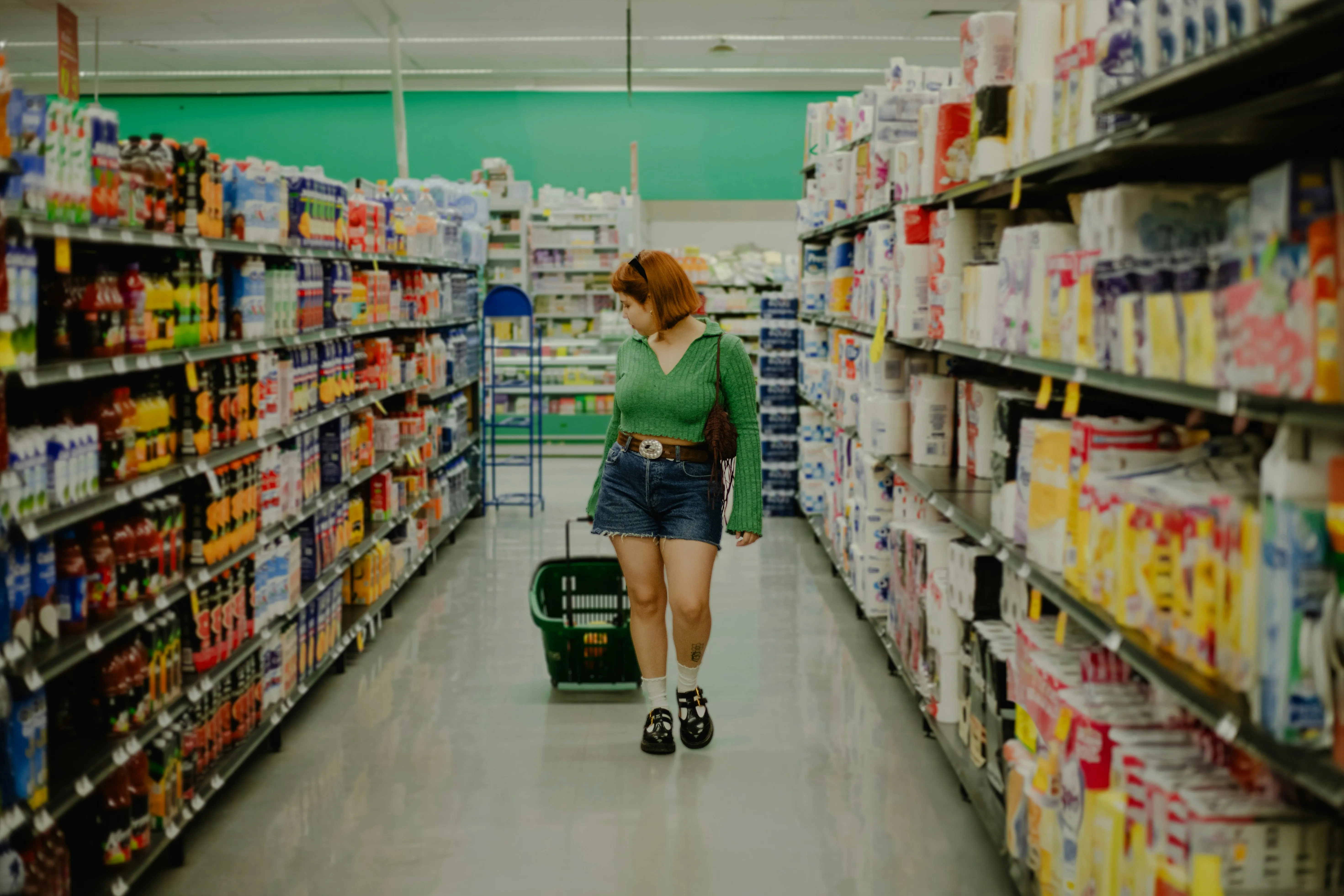 En ung kvinde shopper i Walmart. Hun trækker en lille indkøbskurv bag sig og kigger på varerne på hylderne.