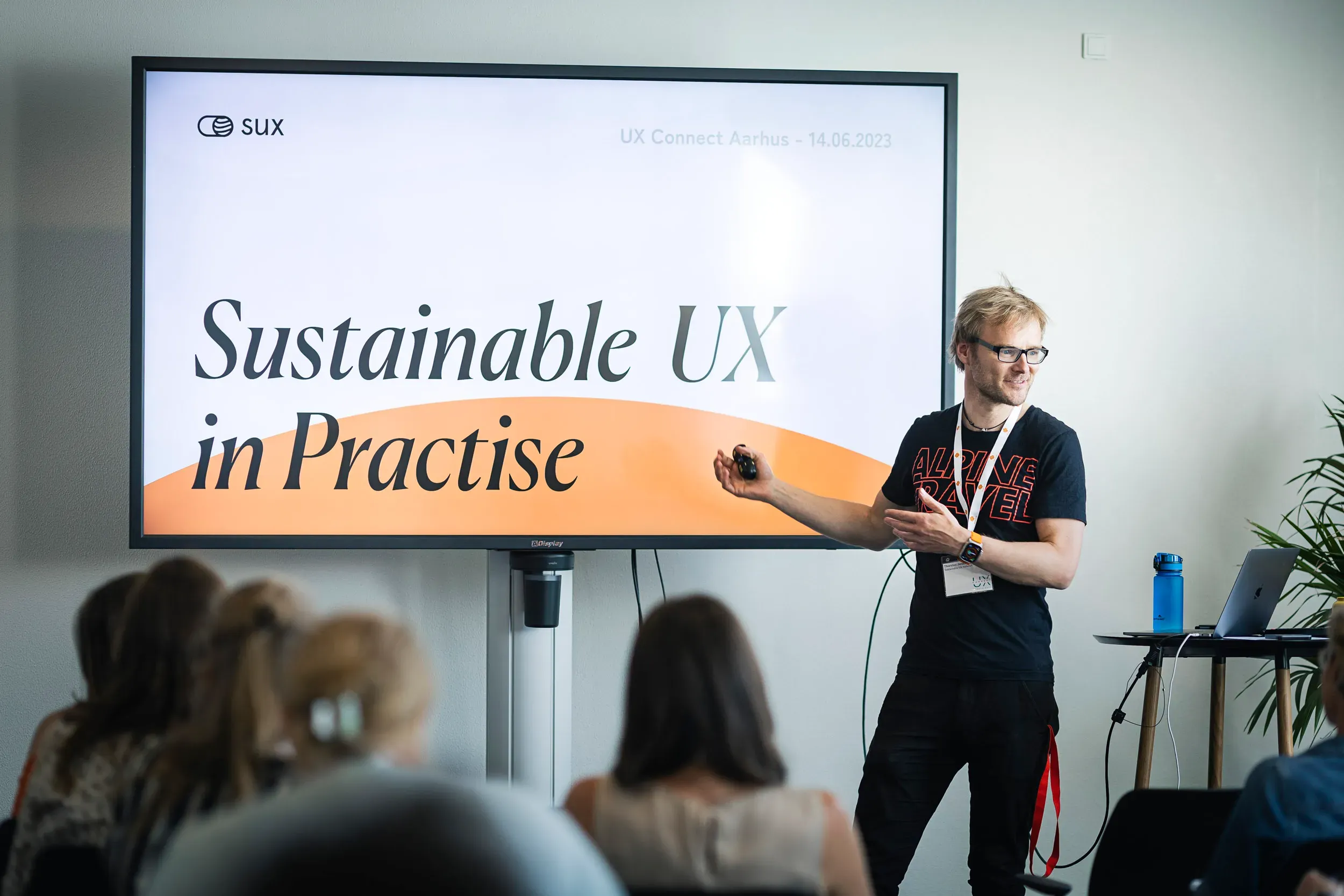Foredrag ved UX Connect Aarhus den 14. juni 2023, hvor en taler præsenterer emnet "Sustainable UX in Practise" med fokus på bæredygtig brugeroplevelse, mens publikum lytter.