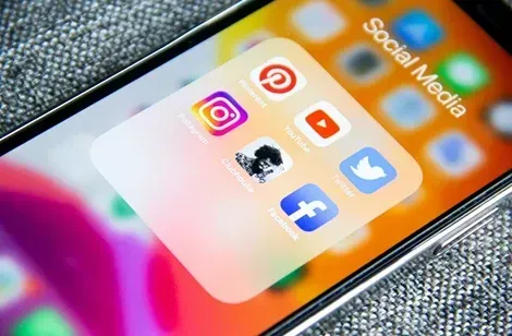 Billede af en smartphone med ikoner for sociale medier: Instagram, YouTube, Pinterest, Twitter og Facebook i en mappe.