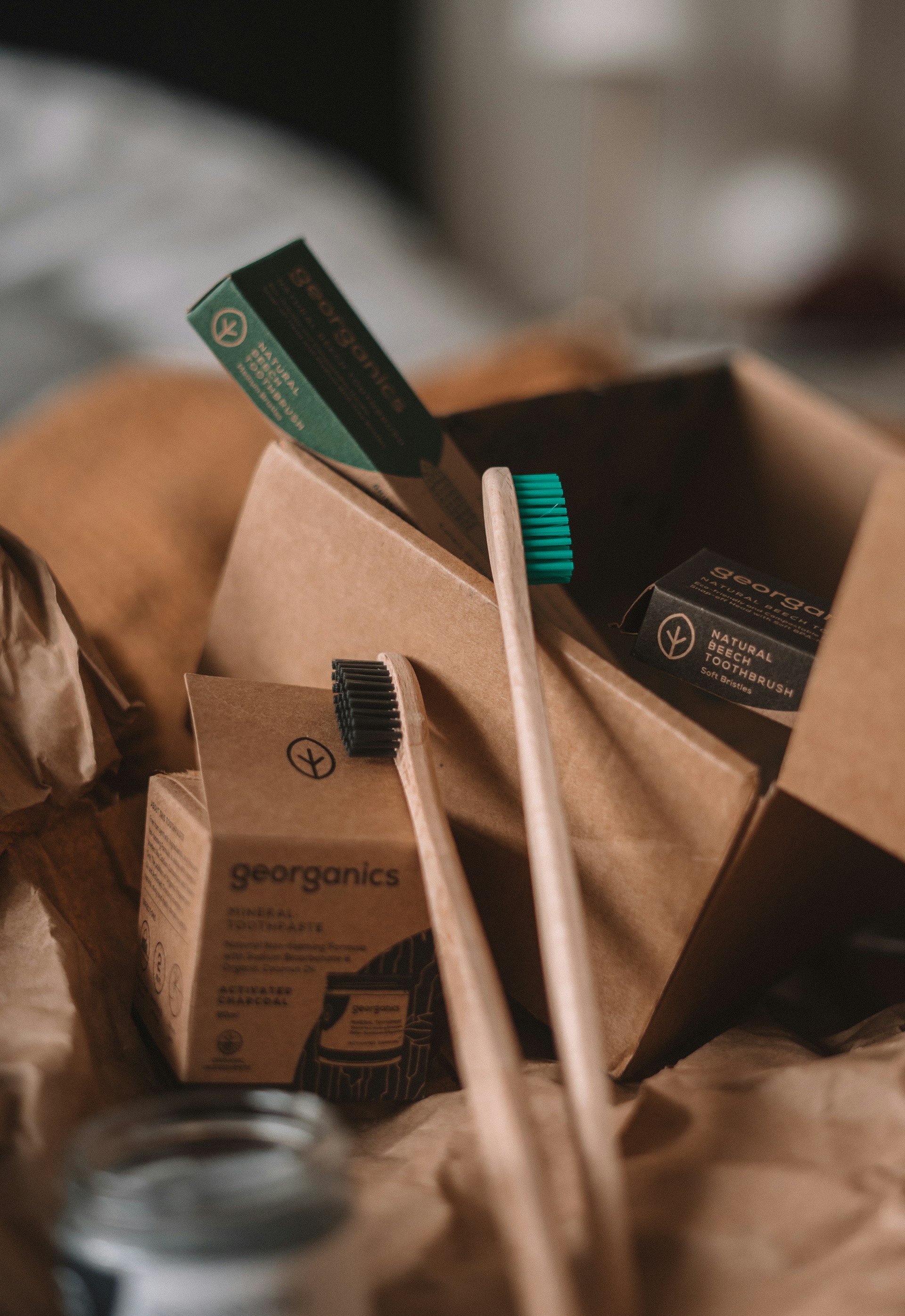 Billede af en naturlig tandbørste og tandpasta fra Georganics, præsenteret i en genanvendelig papkasse omgivet af brunt papir ved siden af en glasbeholder.