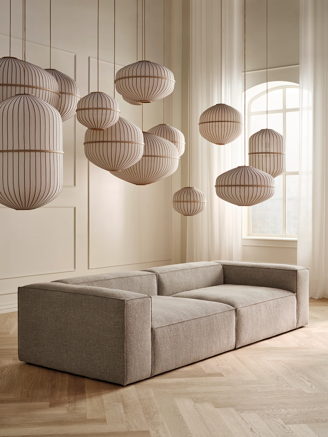 Sofasæt i minimalistisk stil med grå polstring, belejligt placeret under moderne lampedesign i et lyst rum med store vinduer og strømlinede vægge.