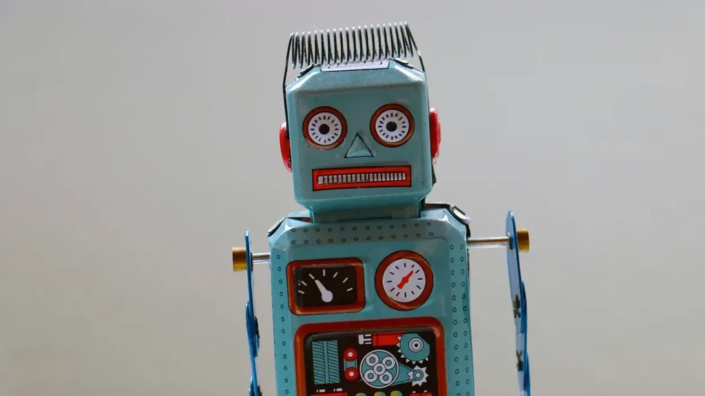 En vintage robotfigur i metal med en blå krop, røde ører og store, runde øjne. Robotten har en skæg frisure, et ur og forskellige mekaniske detaljer på kroppen, der giver et retro-udseende.