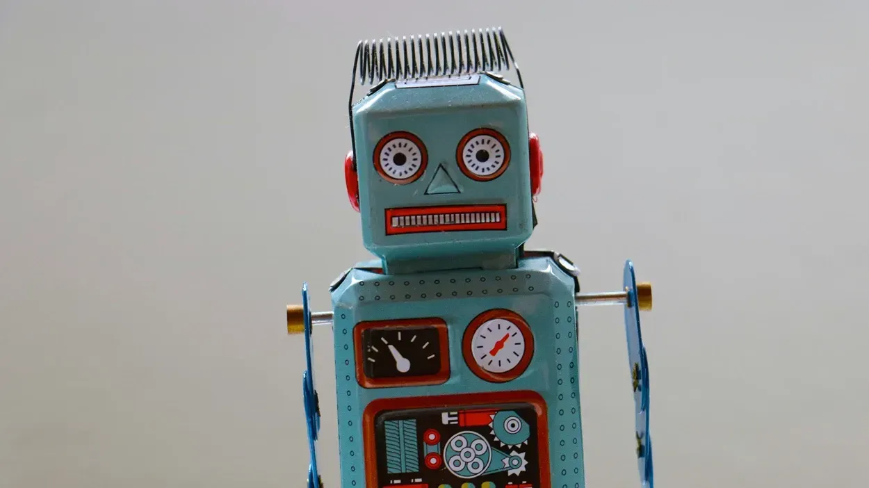 En vintage robotfigur i metal med en blå krop, røde ører og store, runde øjne. Robotten har en skæg frisure, et ur og forskellige mekaniske detaljer på kroppen, der giver et retro-udseende.