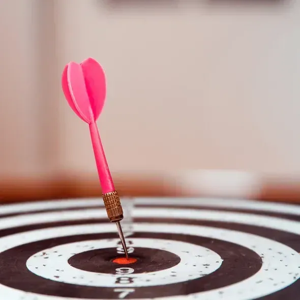 En pink dart der rammer midten af en skydeskive med koncentriske cirkler.