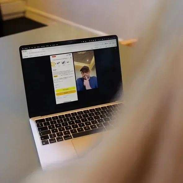 En person ser på en bærbar computer, der viser en videoopkaldsskærm med en mand iført en hat og briller, mens der vises en app med information og en temperatur på 22 grader.