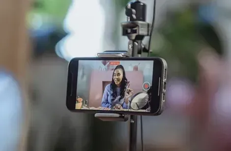 En kvinde optager en video med en smartphone, der er monteret på et stativ, i et lyst og indbydende rum.