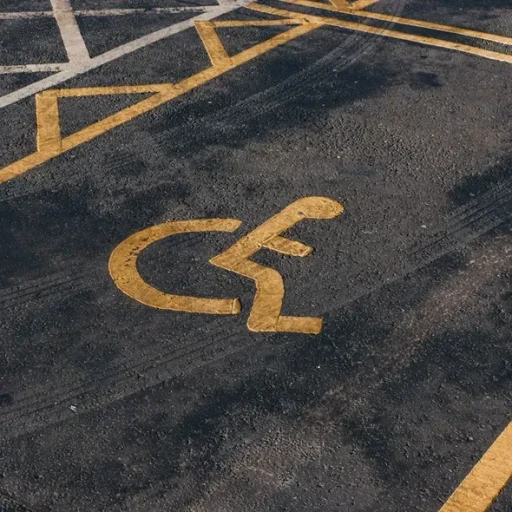 Gul handicap symbols på asfaltparkering, der indikerer plads til handicappede.