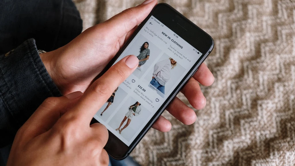 En person holder en smartphone og ser på tøjudvalg i en online butik, mens de navigerer med en finger på skærmen.